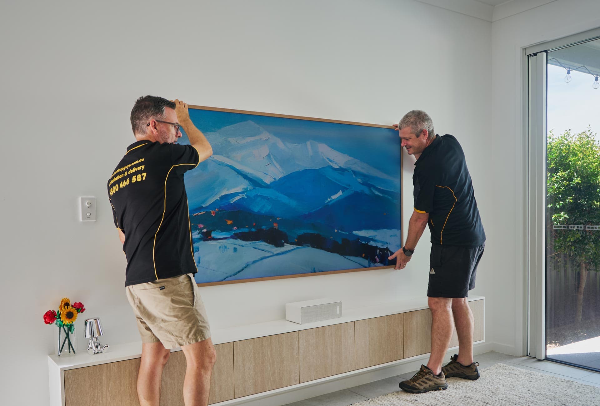 Two installers positioning a large wall-mounted television